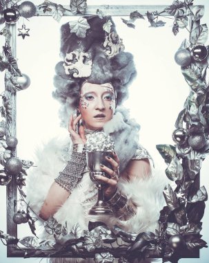 Parti, noel ve halk konsepti: Gümüş sanatsal makyajlı, Noel süslemeleri ile süslenmiş gümüş çerçevede poz veren yaratıcı görünümlü genç kadın. Kış Portresi.