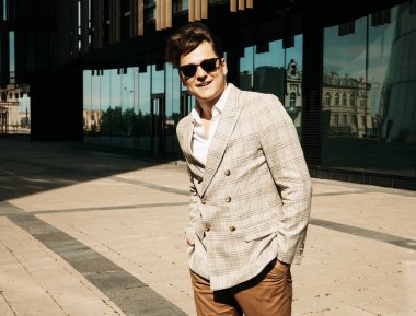 İş dünyası, insanlar ve başarı kavramı: Şaşılası kıyafetli yakışıklı genç iş adamı ve güneş gözlüğü modern ofis yakınlarında yaz mevsiminde yürüyor