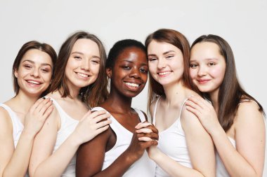 Açık gri arka planda, çok ırklı genç bayan arkadaşlarının portresi. Yaşam tarzı, arkadaşlık ve insan kavramı.