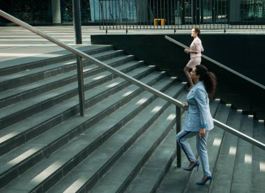 İş, insan ve yaşam tarzı konsepti: Modern ofis binası yakınlarında merdivenleri çıkarken iki genç iş kadını.