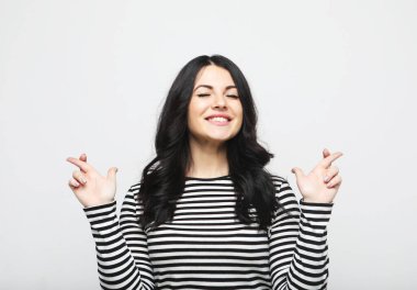 Yaşam tarzı, duygu ve insan konsepti: Neşeli, umutlu ve karizmatik, genç esmer kadın, gri arka planda gerçekleşmek için şans diliyor.