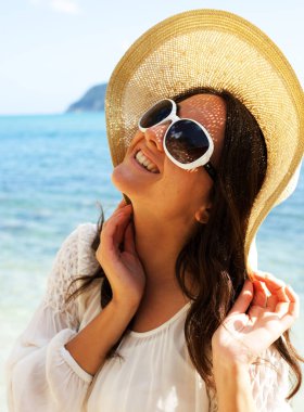 Kapatın. Büyük şapka ve güneş gözlüğü takan mutlu kadın, okyanus kenarında, yaz tatilinde.