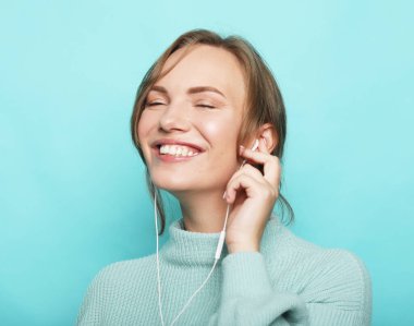 Neşeli genç sarışın kadın gündelik müzik dinliyor kulaklıkları mavi arka planda..