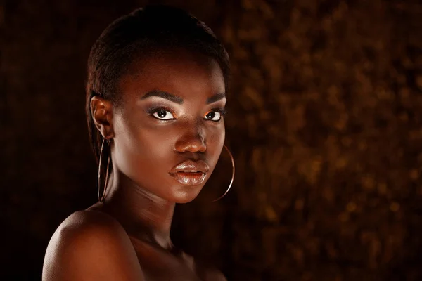 Dark skinned beautiful young woman posing sensually on a golden background. Flawless skin with bright make up.