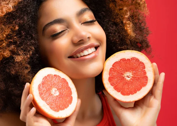lifestyle, food, diet and people concept: Woman holds bright ripe citrus, grapefruit in his hands. Portrait of a female model of Afro appearance. Black hair is curly.