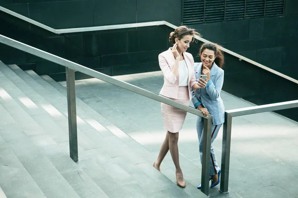 人和技术概念 两位年轻成功的女商人笑着在智能手机上看新闻 利用社交网络 夏天的一天 他们站在街上 在楼梯上 — 图库照片