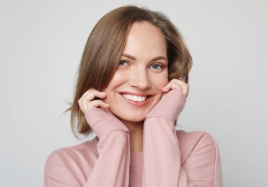 Mutlu, genç, güzel, pembe kazak giyen, gri arka planda gülümseyen, mutlu, sarışın bir kadın..