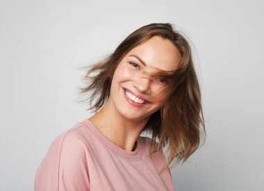 Mutlu, genç, güzel, pembe kazak giyen, gri arka planda gülümseyen, mutlu, sarışın bir kadın..