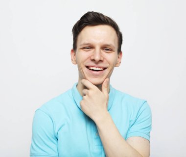 Yaşam tarzı, duygu ve insan konsepti: yakışıklı genç adam gülümsüyor ve açık gri arka planda çenesine dokunuyor