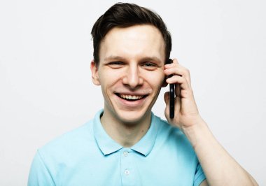 Tahnoloji, duygu ve insan konsepti: genç adam akıllı telefonla konuşuyor ve gri arka plandan kameraya bakıyor