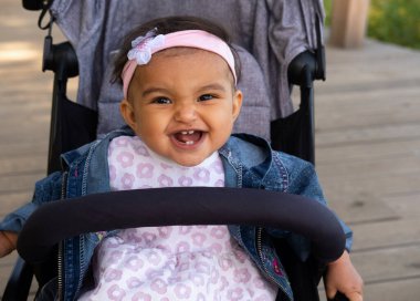 Güzel kız bebek arabasında oturur ve yüksek sesle güler, açık havada, yakın planda.