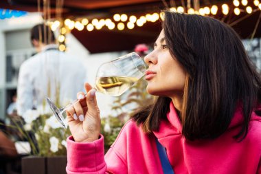 Pembe kazaklı güzel bir Asyalı kadın açık havada, bir yazlık kafede beyaz şarap içiyor. Yaşam tarzı kavramı.