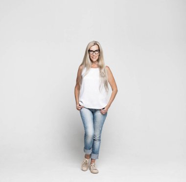 Kotlar, beyaz bluzlar ve açık gri arka planda poz veren uzun beyaz saçlı gözlüklü şık, yaşlı bir kadının tam boy fotoğrafı. Moda konsepti.