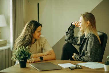 Günlük kıyafetli iki genç kadın ofiste iletişim kuruyor, iş tartışıyorlar..