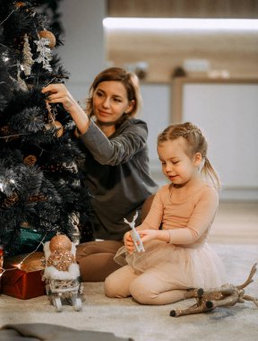 Aile, kış tatilleri ve insanların konsepti. Mutlu anne ve küçük kız evde Noel ağacı süslüyorlar.