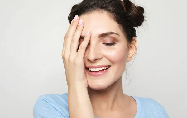 A beautiful young woman with dark hair in a blue t-shirt covers her eye with her palm and laughs. Charming smile. The concept of happiness and well-being.