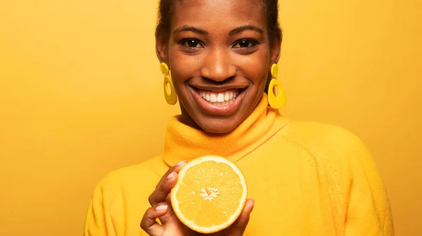 lifestyle, food, diet and people concept: Photo of young afro american woman hold orange slices look amazed isolated on yellow color background.
