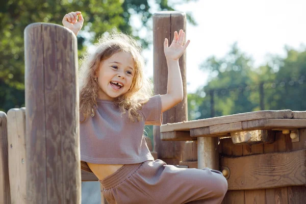 Summer children\'s games and fun outdoors. Happy child girl with blond gurly hair play on wooden playground on sunny day. Lifestyle and childhood concept.