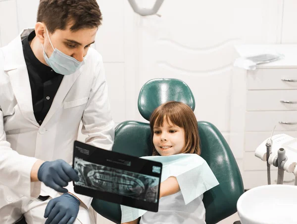 口腔医学 技术和保健概念 在牙科诊所办公室向女童展示牙齿X光的男牙医 — 图库照片