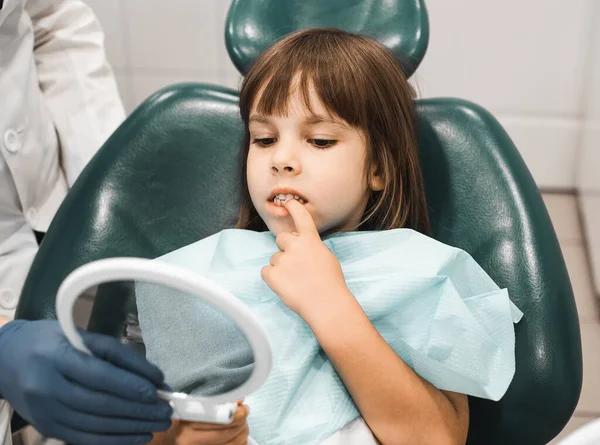 Little child Girl seating in dental office and looking at her teeth the mirror. People, medicine, stomatology, technology and health care concept.