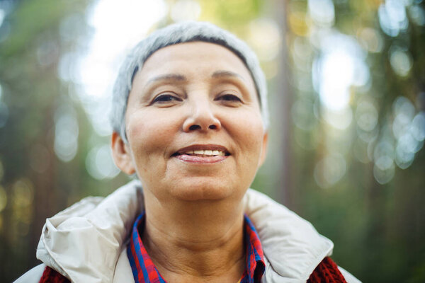 Portrait of a smiling elderly Asian woman with short gray hair in the park. Autumn day.
