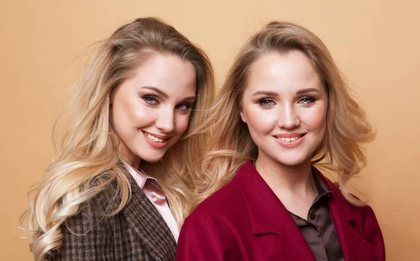 2人の女の子の積極的な肖像画 冬のスタイリッシュなコートを着てベージュの背景に屋内をポーズ親友 ファッショナブルな服 姉妹双子 — ストック写真