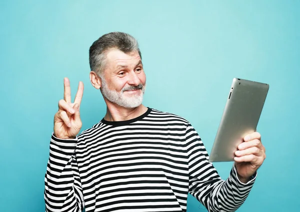 ライフスタイル テクノロジー 高齢者の概念 魅力的な高齢者の男性は青の背景にデジタルタブレットを使用して友人と通信します ストックフォト