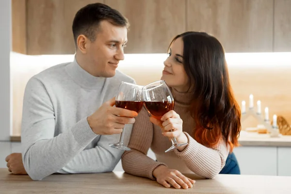 ロマンチックな美しい若いですカップル保持眼鏡で立って現代的な居心地の良いキッチンルームインテリア 幸せな結婚した男の夫と女の子妻飲む赤ワインお祝いで一緒に家 ロイヤリティフリーのストック画像