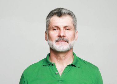 Gri arka planda izole edilmiş yeşil tişört giyen yaşlı, yaşlı, beyaz bir adamın portresi..