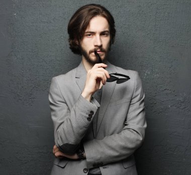 Yaşam tarzı, duygu ve insan konsepti: Gri arka planda kameraya bakan, şık saç stili ve sakallı genç sakallı adam.