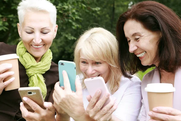 Three Elderly Women Smiling Looking Photos Screen Phones Park Summer — Foto de Stock
