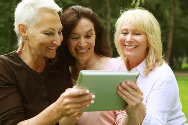 Три Пожилые Женщины Улыбаются Смотрят Новости Экран Планшета Парке Летний — стоковое фото