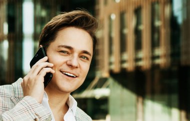 İş dünyası, insanlar, tehnoloji ve yaşam tarzı konsepti: Genç yakışıklı iş adamı dışarıda telefonla konuşuyor