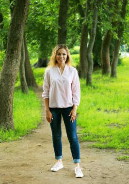 Uzun sarı dalgalı saçlı, genç ve güzel bir kadın. Yaz günü. Parkta tam boy portre.