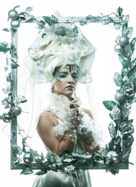 Parti, Noel ve insanlar: Noel karnavalı için kostüm giymiş güzel bir kadın Noel süslemeleri ve gümüş yapraklar çerçevesinde poz veriyor. Yaratıcı makyaj, saç stili.