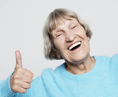 Yaşam tarzı, duygu ve insan konsepti: Yaşlı mutlu kadın başparmağını kaldırıyor ve kameraya bakıyor