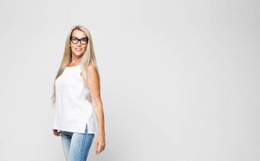 Kotlar, beyaz bluzlar ve açık gri arka planda poz veren uzun beyaz saçlı gözlüklü şık, yaşlı bir kadının tam boy fotoğrafı. Moda konsepti.