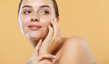 Temiz tenli güzel genç bir kadın bej arka planda yüzüne dokunuyor. Kozmetik, güzellik ve kaplıca konsepti.