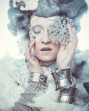 Parti, noel ve halk konsepti: Yeni yıl tarzında yaratıcı makyajlı genç güzel bir kadın yüzünde gümüş kar taneleri tutuyor. Kar Kraliçesi, peri.