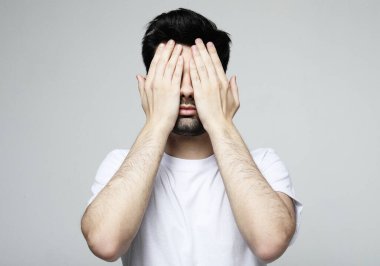 Genç, yakışıklı, sakallı adam gri arka planda gözlerini kapatıyor.