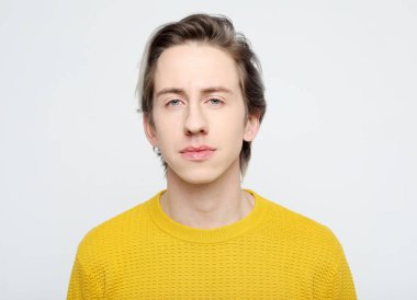 Yaşam tarzı, duygu ve insan konsepti: yakışıklı genç adam gri arka planda kameraya bakarken sarı kazak giyiyor