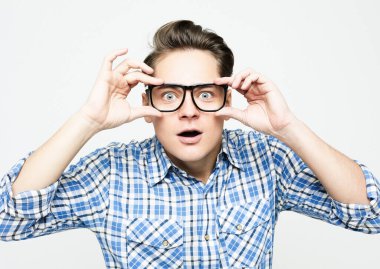 Mavi günlük ekose gömlek ve gözlük giyen genç adam beyaz arka planda heyecanlı bir yüz görünce şaşırdı ve şok oldu.