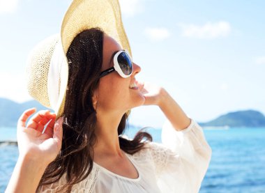 Sahilde hasır şapkalı ve güneş gözlüklü genç bayan, mutlu tatiller.