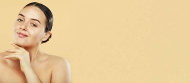 Young brunette female with shiny highlighters and glossy lips touching her chin, pretty woman with natural make up and perfect hairstyle. Beauty concept. Copy space.