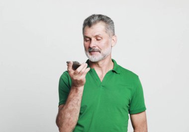 Teknoloji, yaşlılar, yaşam tarzı ve iletişim konsepti. Yaşlı adam gri arkaplan üzerinden sesli mesaj göndermek için akıllı telefon kullanıyor..
