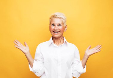 Yaşlılar, modern yaşam tarzı, vücut dili kavramı. Şok olmuş, kısa beyaz saçlı, sarı arka planda izole edilmiş kameraya bakan olgun bir kadının yakın plan portresi.