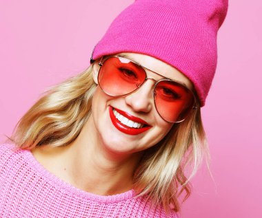 Pembe pulover ve şapka giymiş, pembe arka planda poz veren modaya uygun genç kadın portresi. Hipster tarzı.