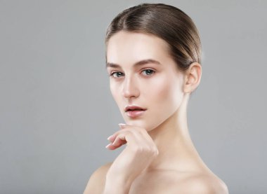 Temiz tenli güzel genç bir kadın gri arka planda yüzüne dokunuyor. Kozmetik, güzellik ve kaplıca konsepti.