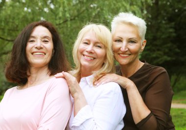 Yaşlılar, dostluk ve duygu kavramı: Üç güzel yaşlı bayan parkta sarılıyor. Sıradan giyinmiş kadınlar eğlenir ve mutlu olurlar..