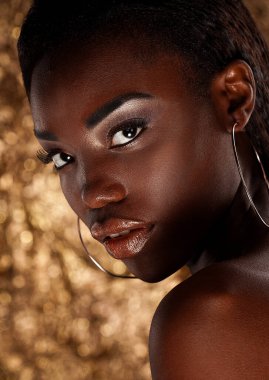 Parlak makyajlı güzel bir Afrikalı kadın altın bir arkaplanda poz veriyor..